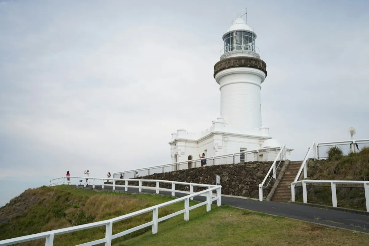 A white lighthouse on a grassy headland with a fenced path