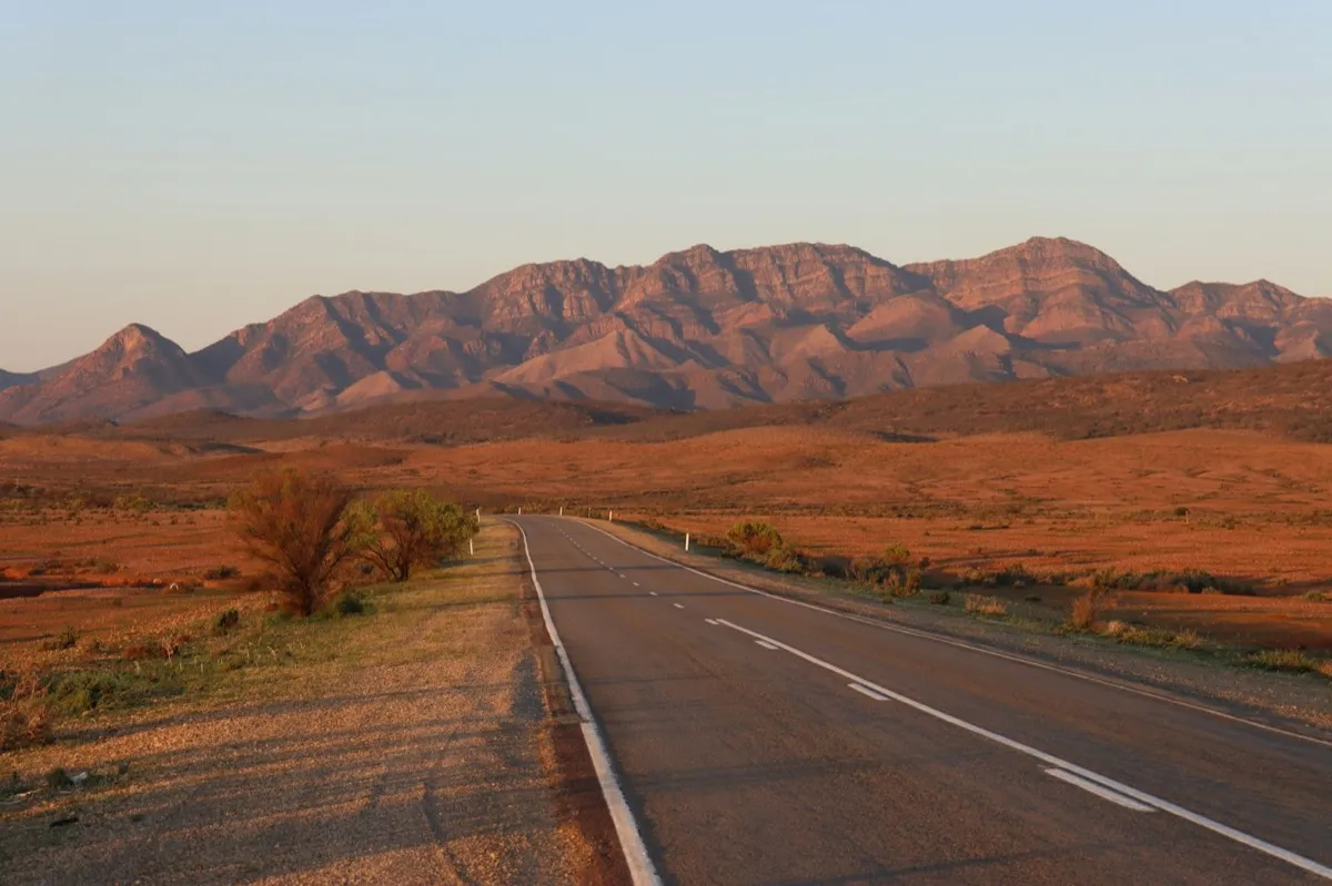 A highway running towards red mountains through dry scrub