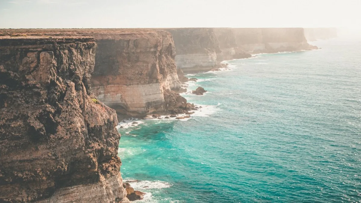 Sheer cliffs dropping into turquoise sea along a long, flat coastline