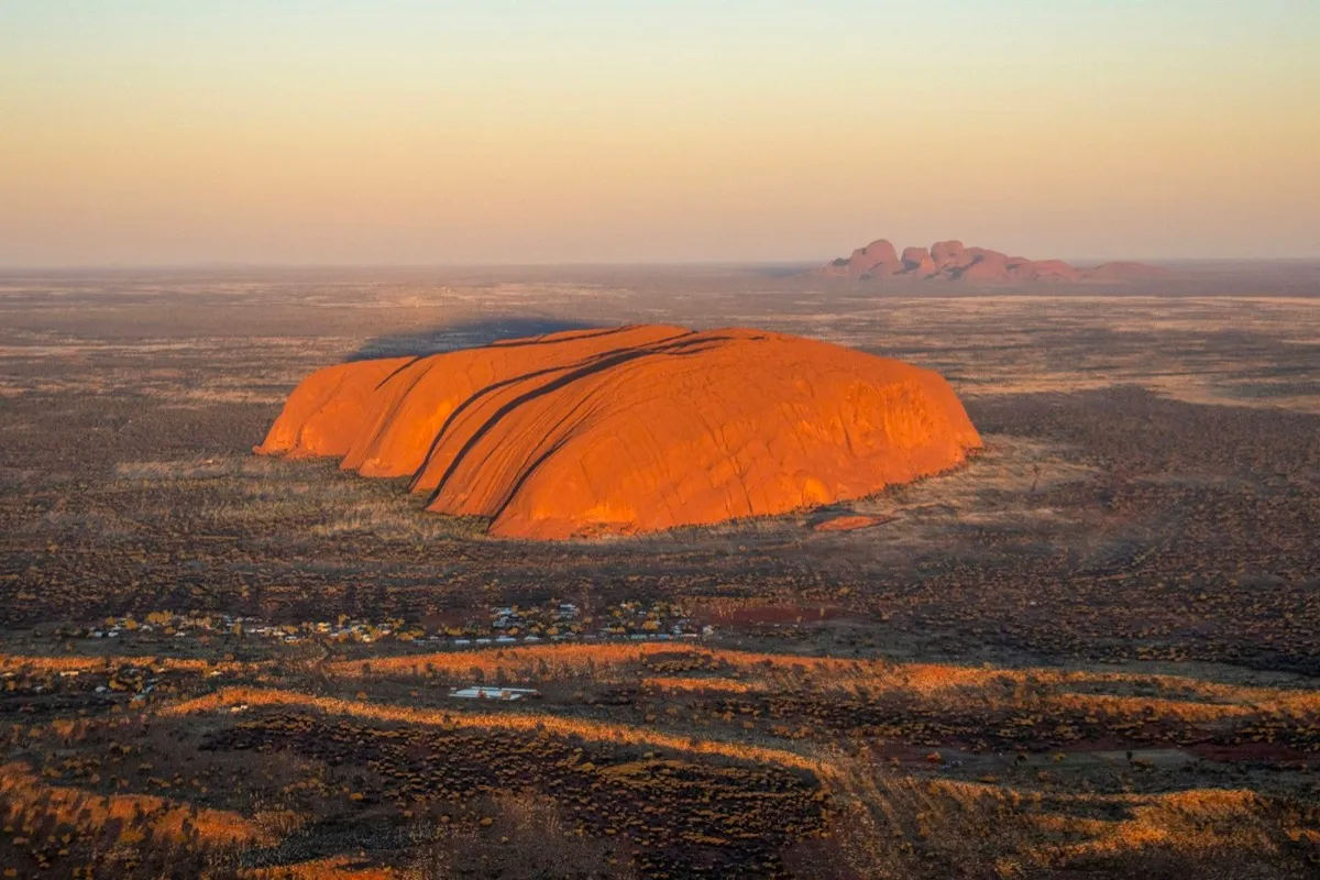 Aerial view of Uluru glowing at sunset with Kata Tjuta on the horizon
