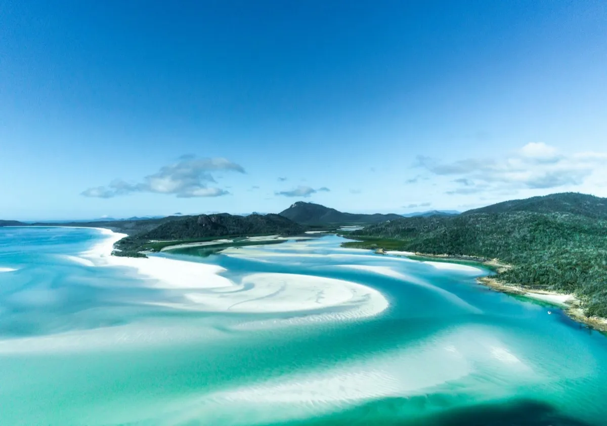 Swirls of white sand and turquoise water below green hills